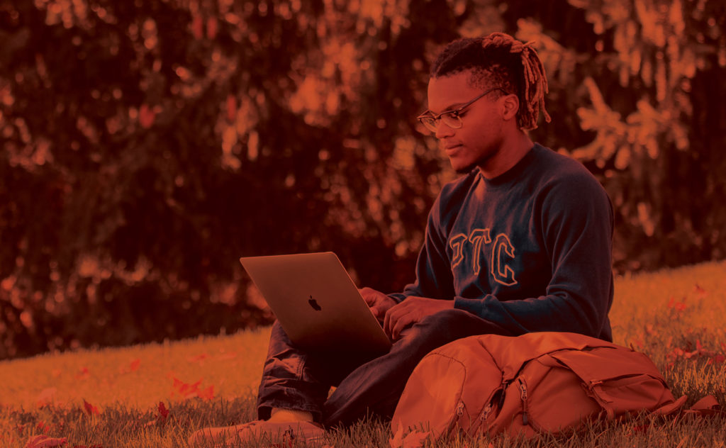 student sitting in the grass with a laptop