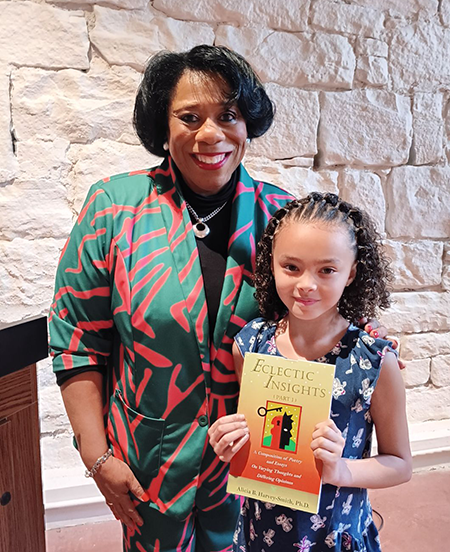 A photo of Dr. Harvey-Smith standing with a young girl named Dakota who is holding Dr. Harvey-Smiths book "Eclectic Insights".